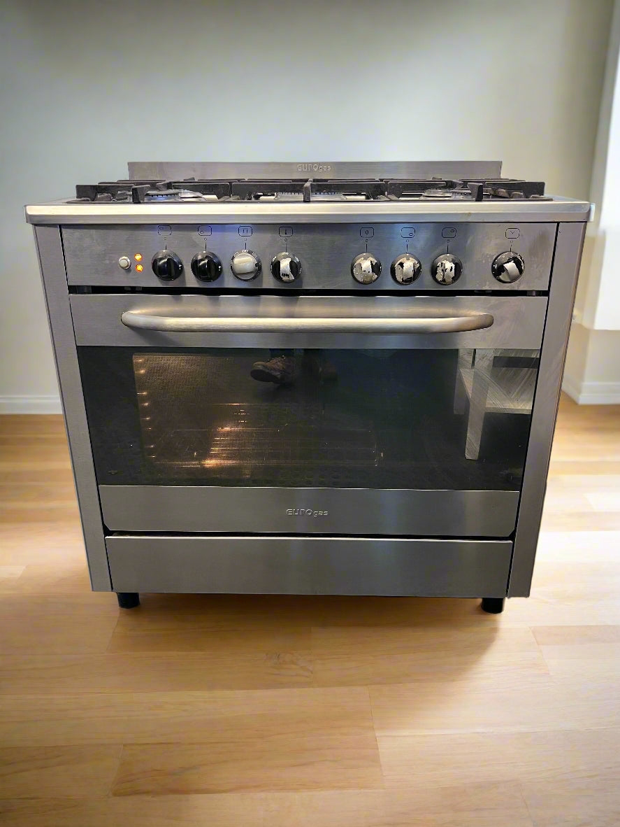 Stainless steel kitchen stove with gas cooktop on a wooden floor.