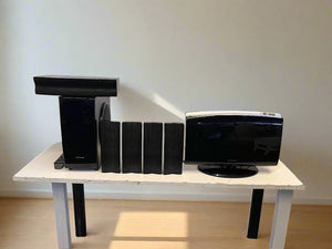 Black home theater system on a white table against a plain wall.