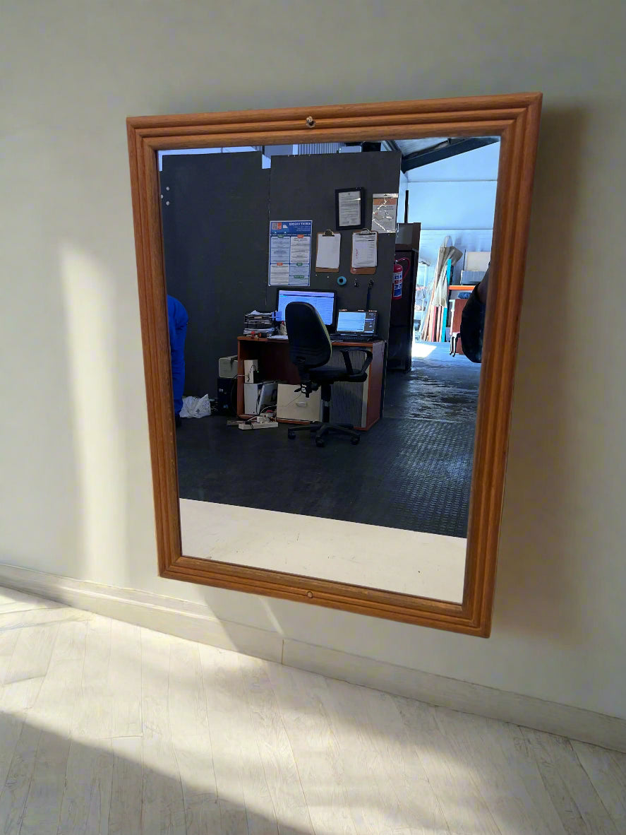Wooden-framed mirror on a wall reflecting an office desk with computers.
