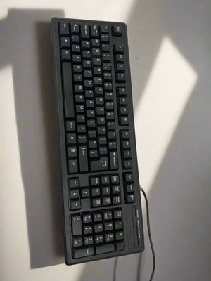 Black keyboard on a light gray surface with shadows cast by the keys