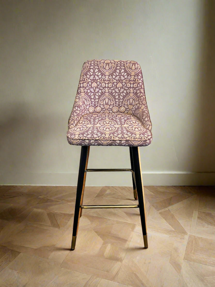Bar stool with patterned pink seat on a wooden floor against a plain wall