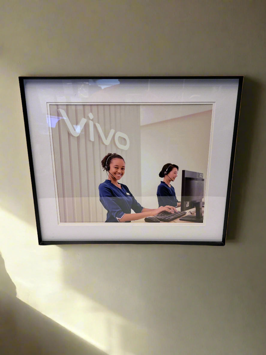 Framed picture of two women working on computers with 'vivo' branding.