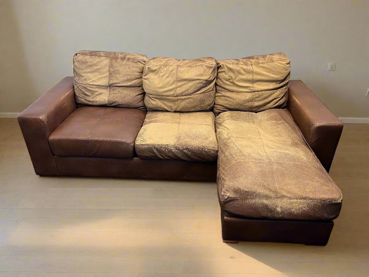 Brown sectional sofa in a room with a plain wall and floor.