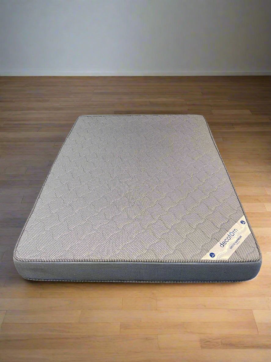 Gray mattress on a wooden floor with a plain wall background