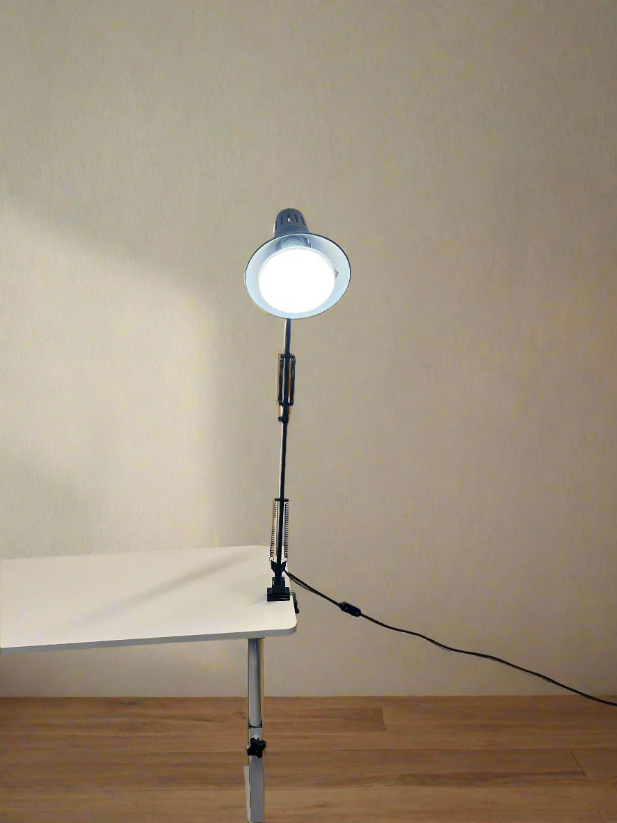 Portable lamp on a stand with a white light bulb against a plain wall.