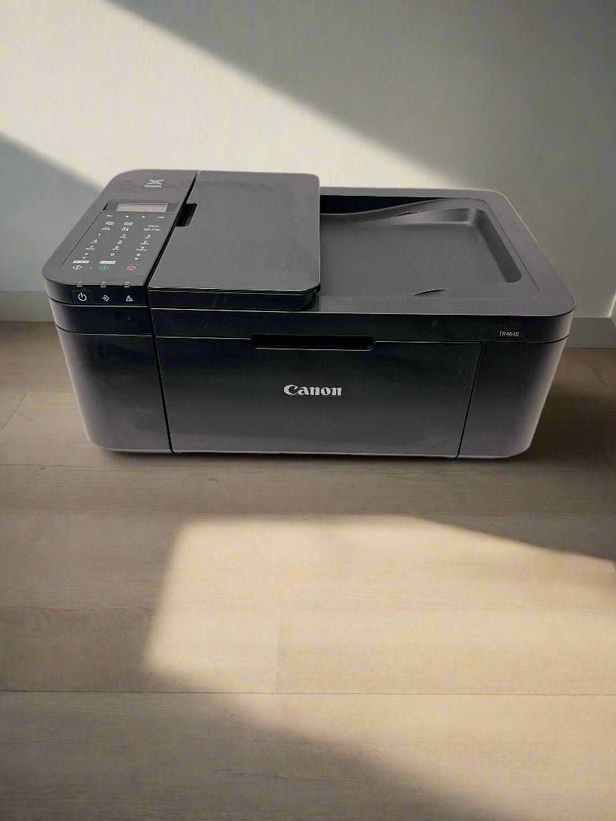 Black Canon printer on a white surface with a gray brick wall background