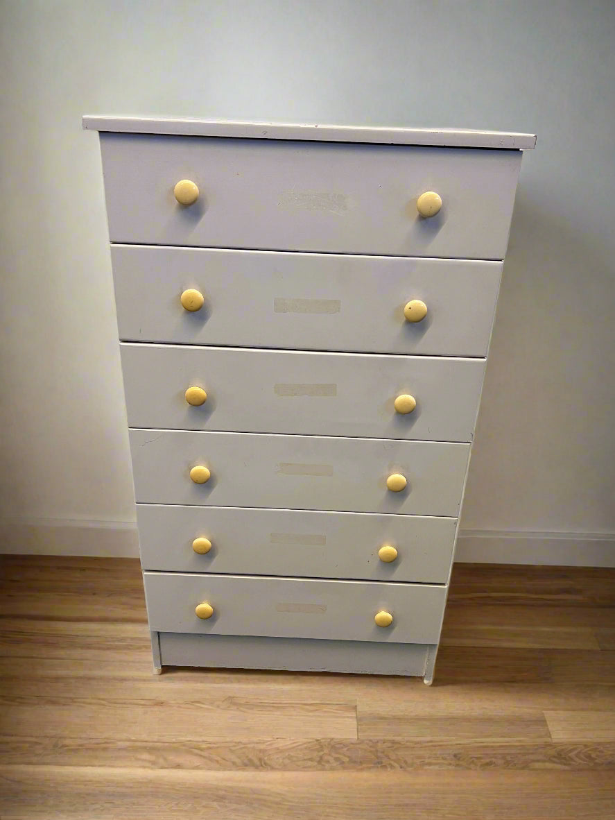 White dresser with yellow knobs on a wooden floor against a plain wall
