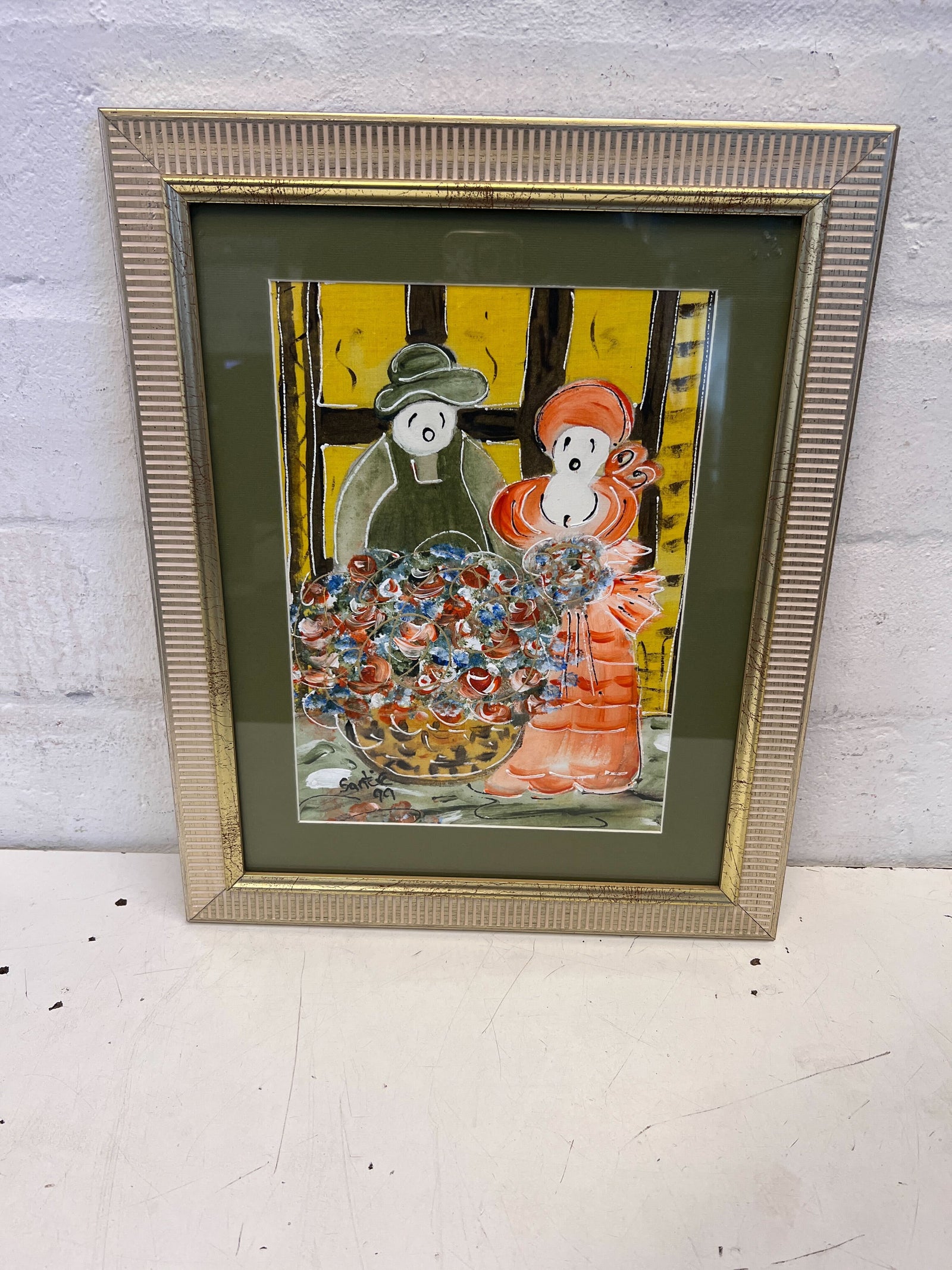 Framed artwork of two figures with a basket on a white surface