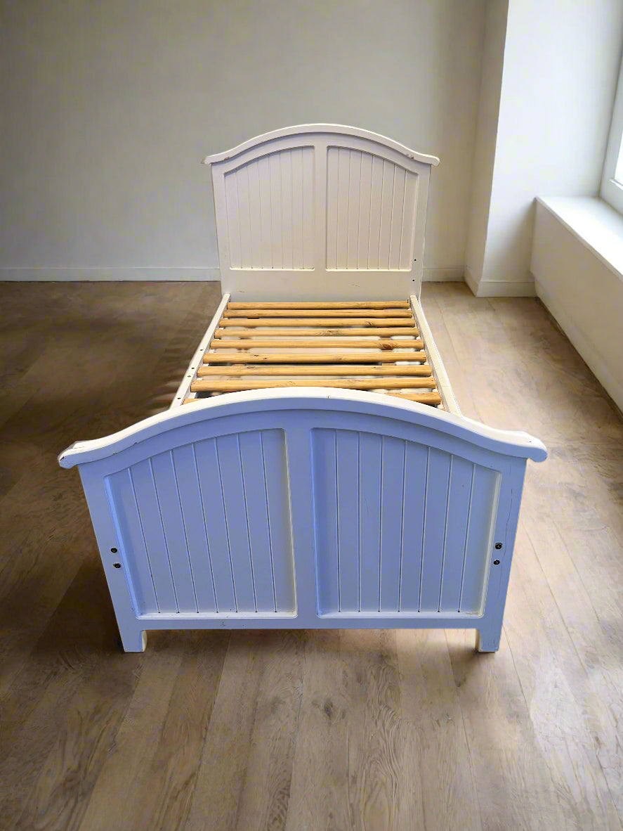 White wooden bed with slatted headboard on a wooden floor.