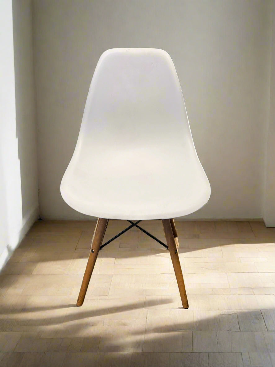 White chair with wooden legs on a light wooden floor against a white wall