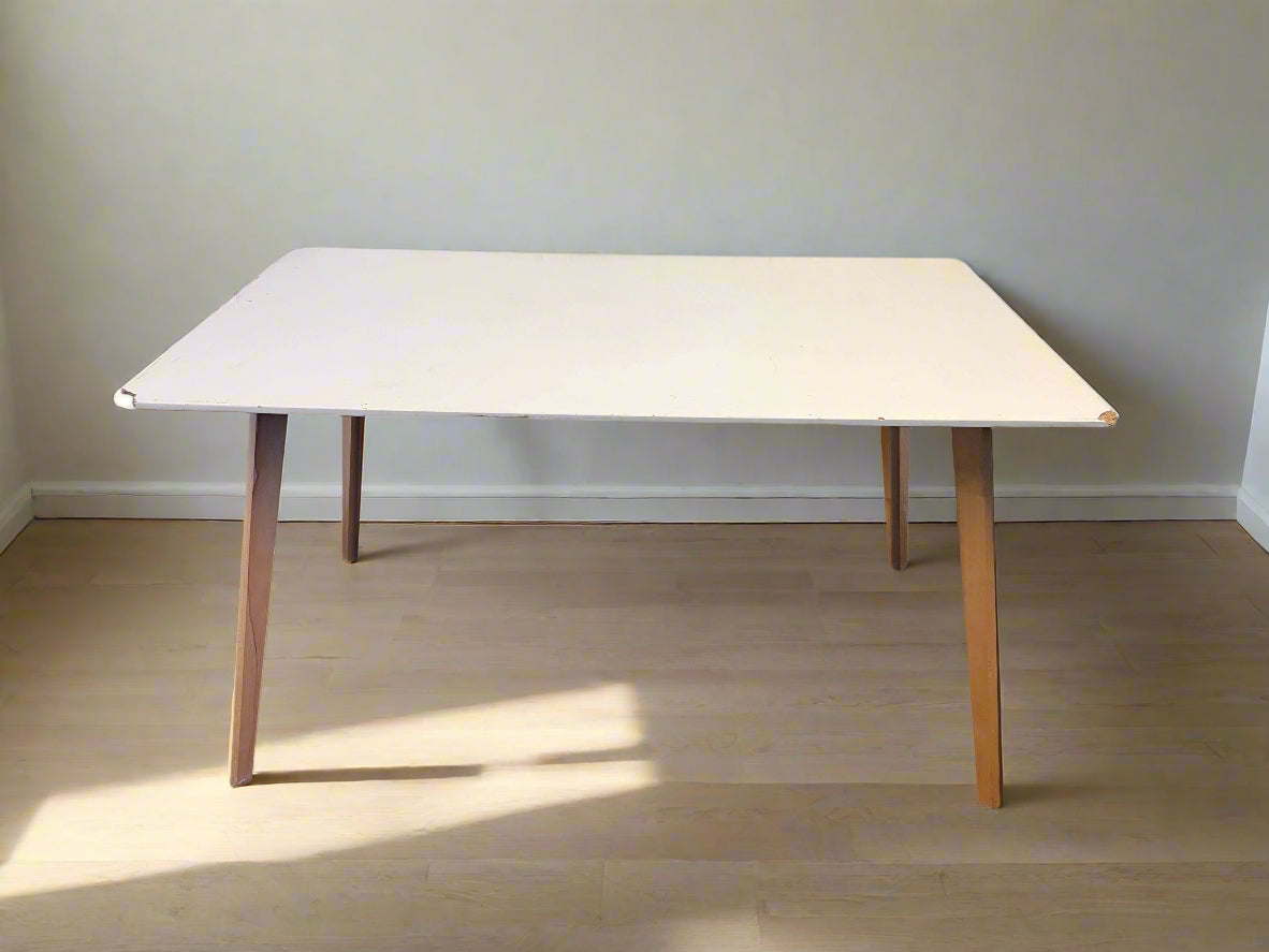 White table with wooden legs on a plain floor and wall background
