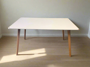 White table with wooden legs on a plain floor and wall background