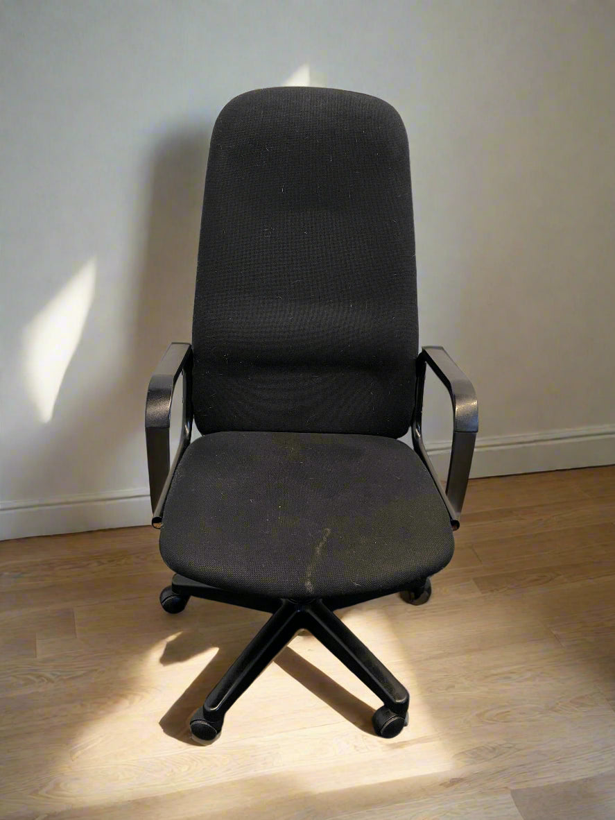 Black office chair with visible wear on a wooden floor against a white wall