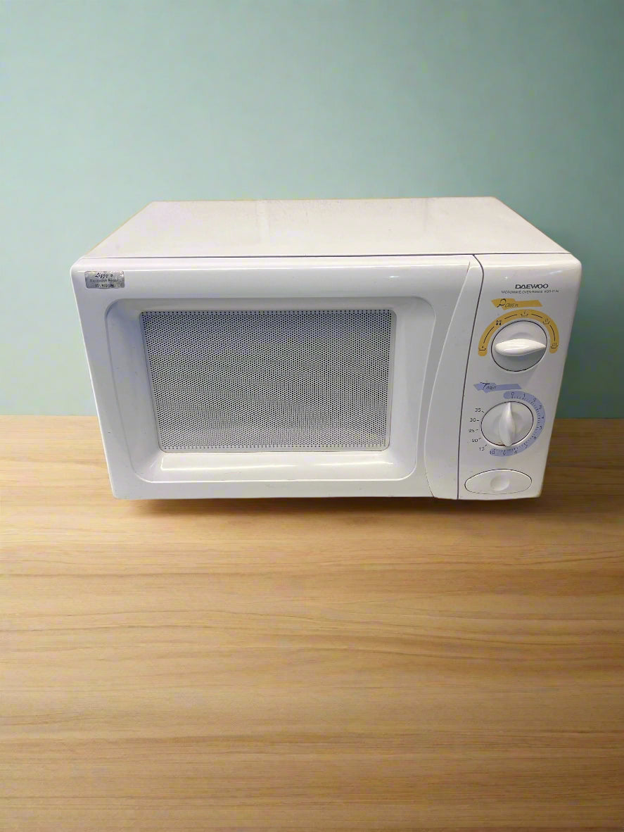 White microwave oven on a white surface with a gray brick wall background