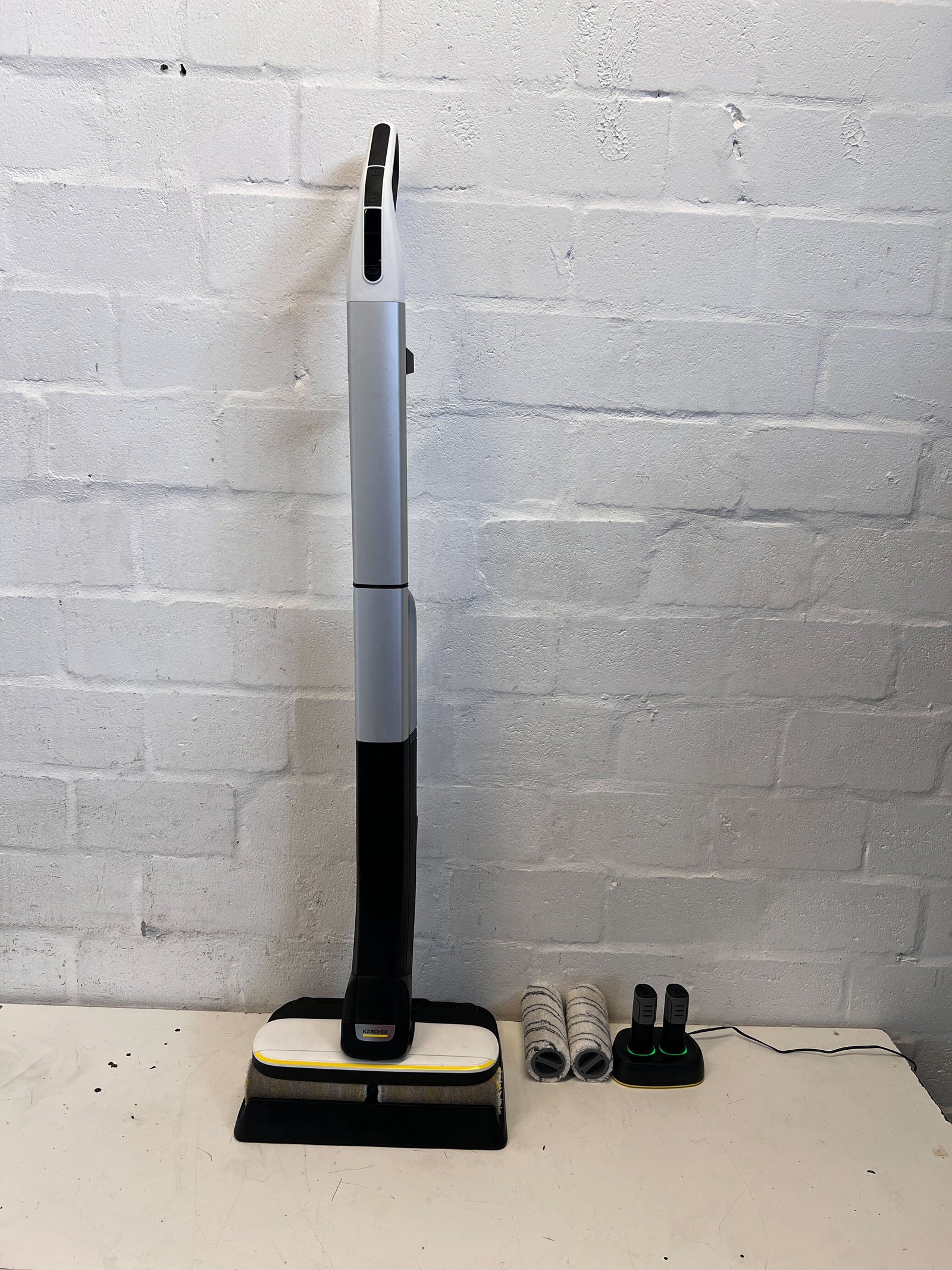 Cleaning device with attachments on a white surface against a white brick wall
