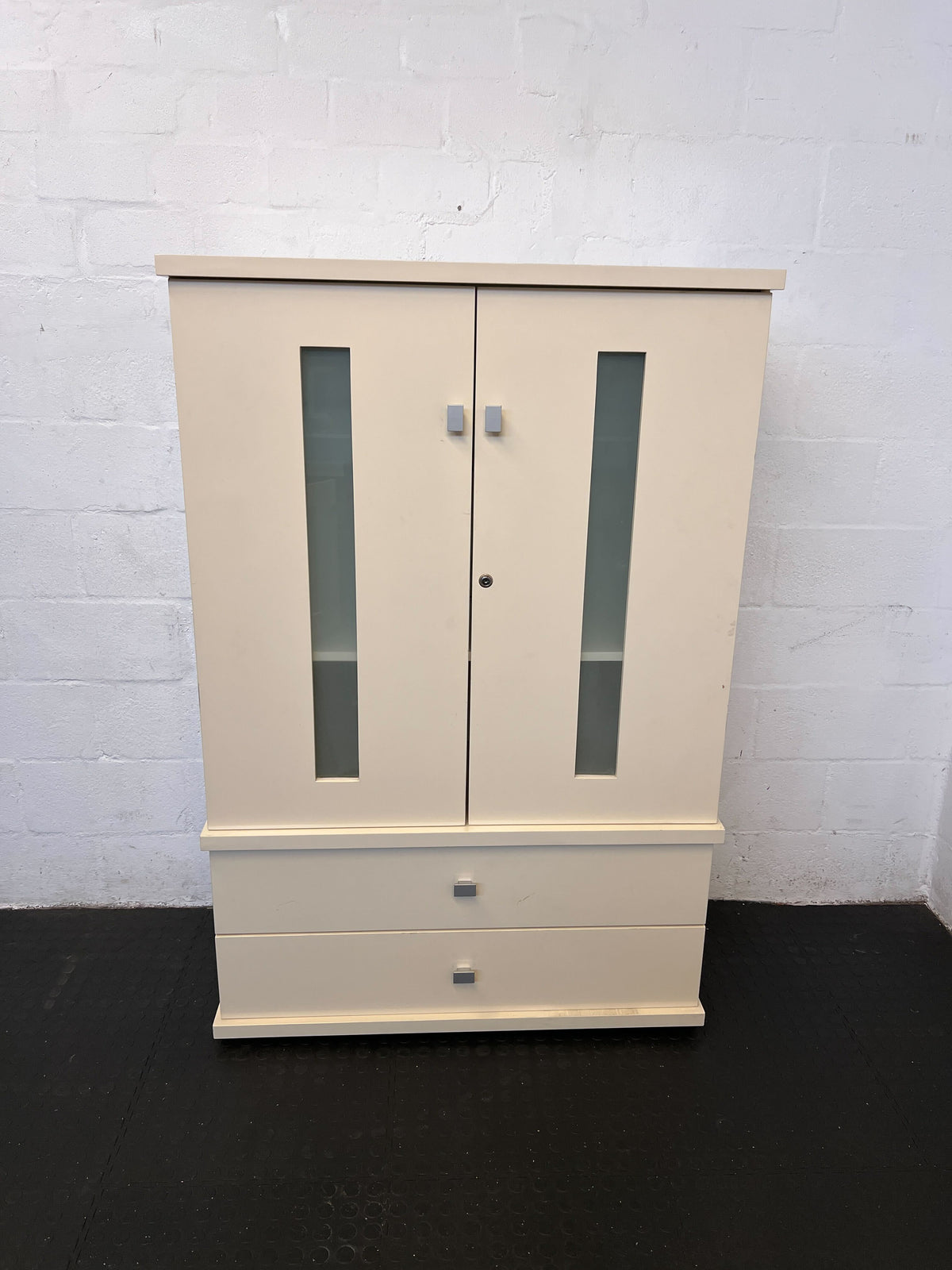 Beige wardrobe with glass panels against a white brick wall.