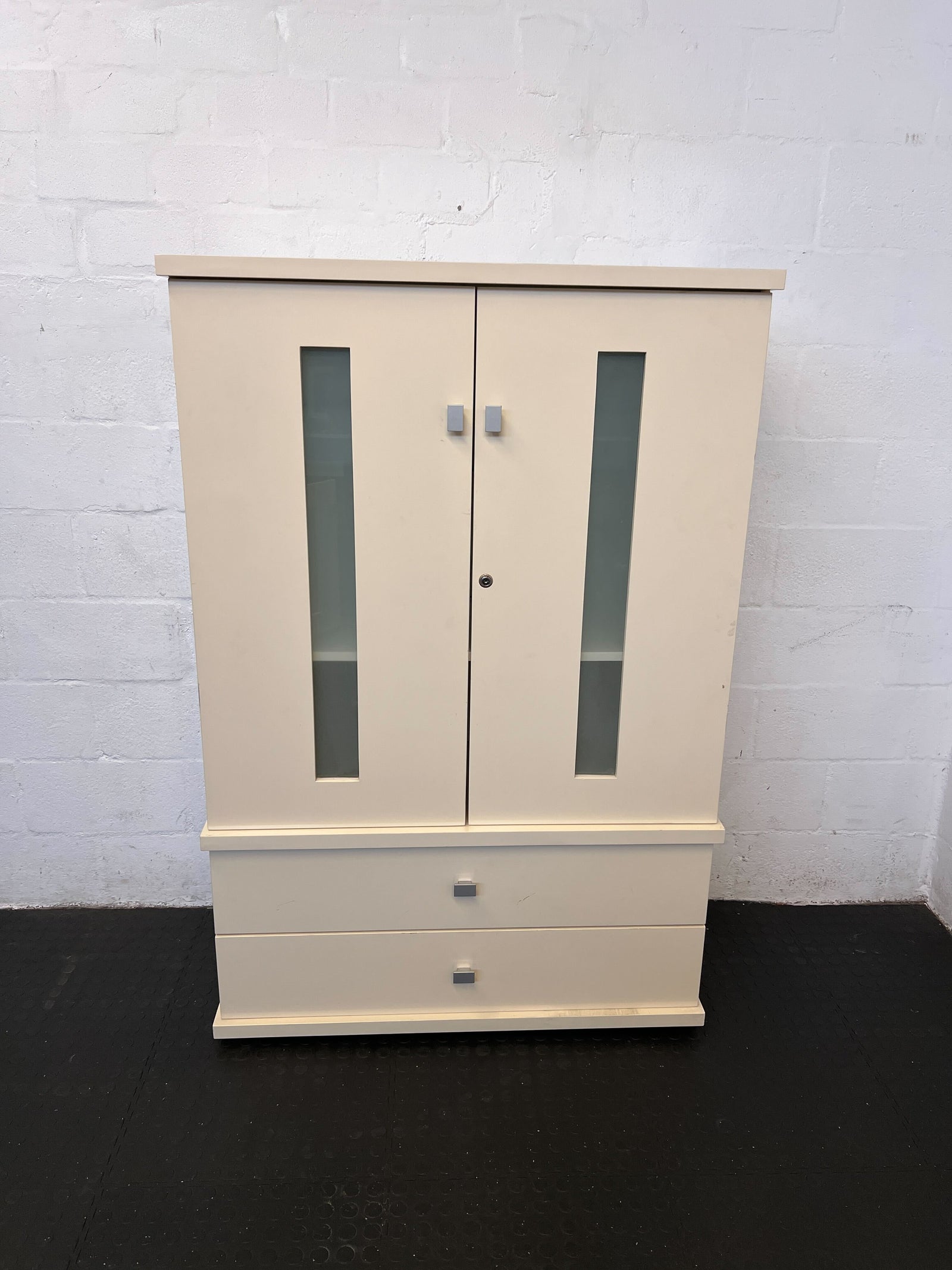 Beige wardrobe with glass panels against a white brick wall.