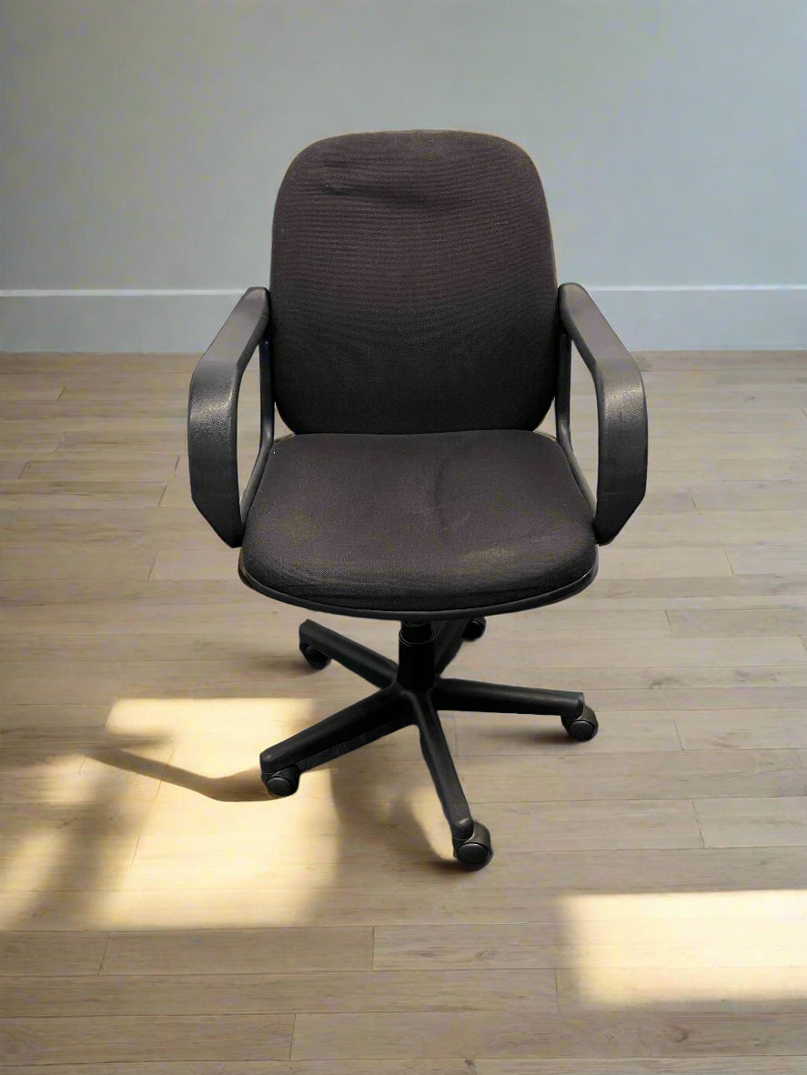 Black office chair against a light gray brick wall.