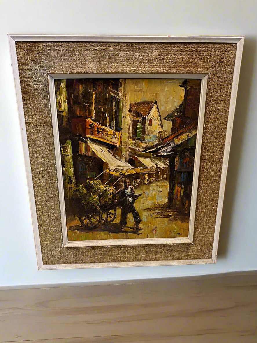 Framed painting of a street scene with a man and cart on a white wall.