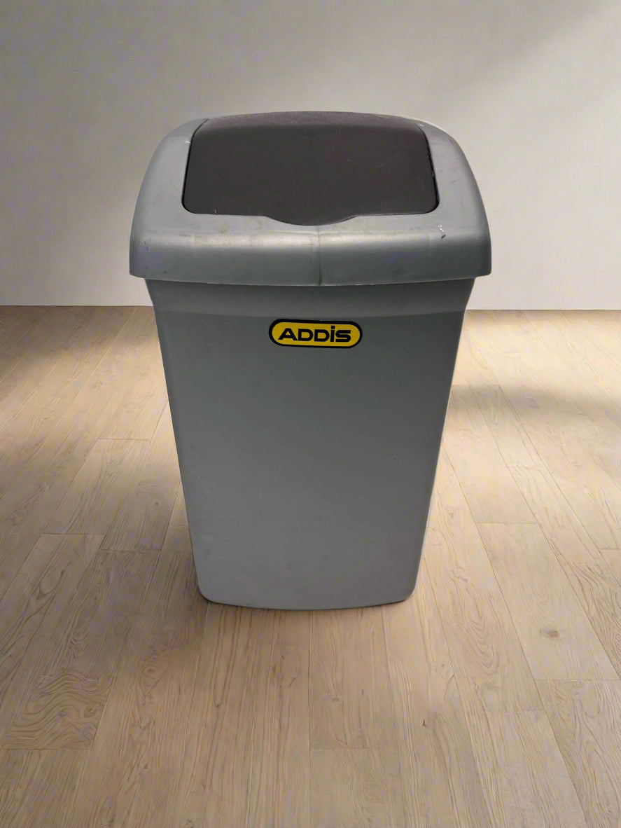 Gray trash bin with a black lid on a light gray floor and background