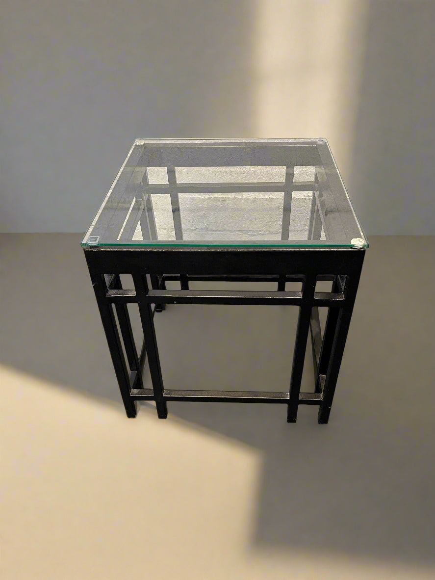 Glass top table with black metal frame on a plain background