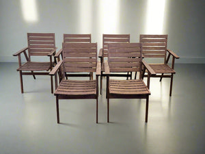 Set of six wooden chairs against a white brick wall.