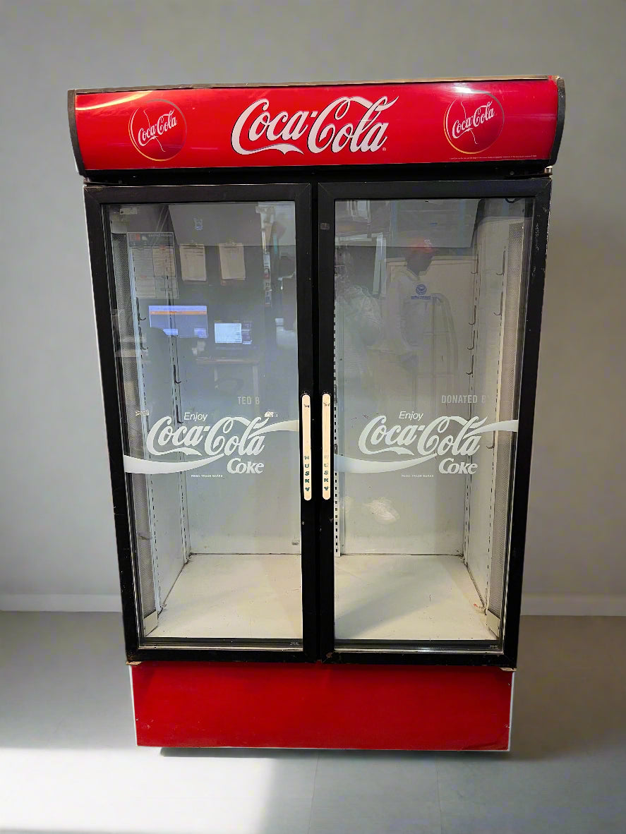 A vintage double glass door refrigerator with red and black exterior, branded with Coca-Cola.