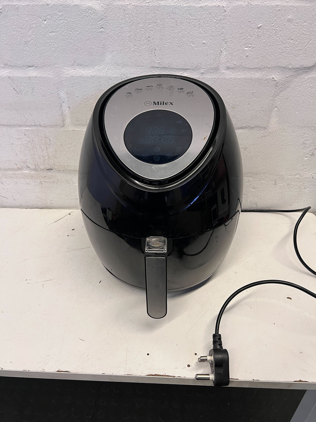 Black air fryer on a white surface with a white brick wall background
