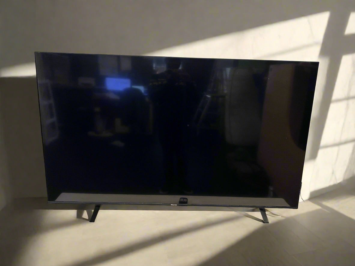 Flat-screen TV on a stand with a remote control in front of a white brick wall