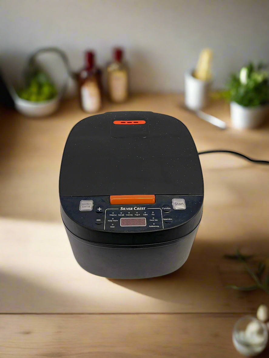 Black rice cooker on a white surface with a gray brick wall background