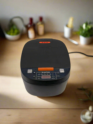 Black rice cooker on a white surface with a gray brick wall background