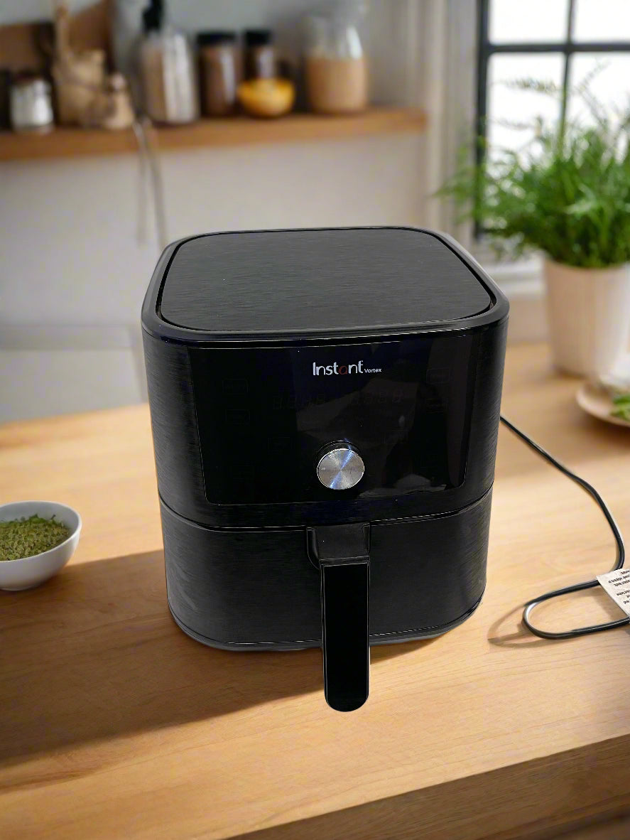 Black air fryer on a white surface with a gray brick wall background