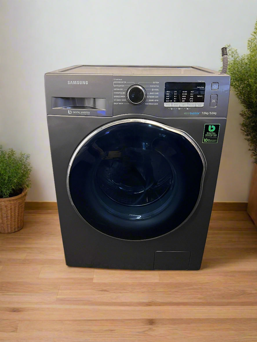 Samsung washing machine on a wooden floor with plants on either side.