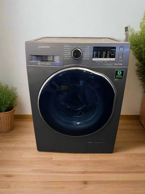 Samsung washing machine on a wooden floor with plants on either side.
