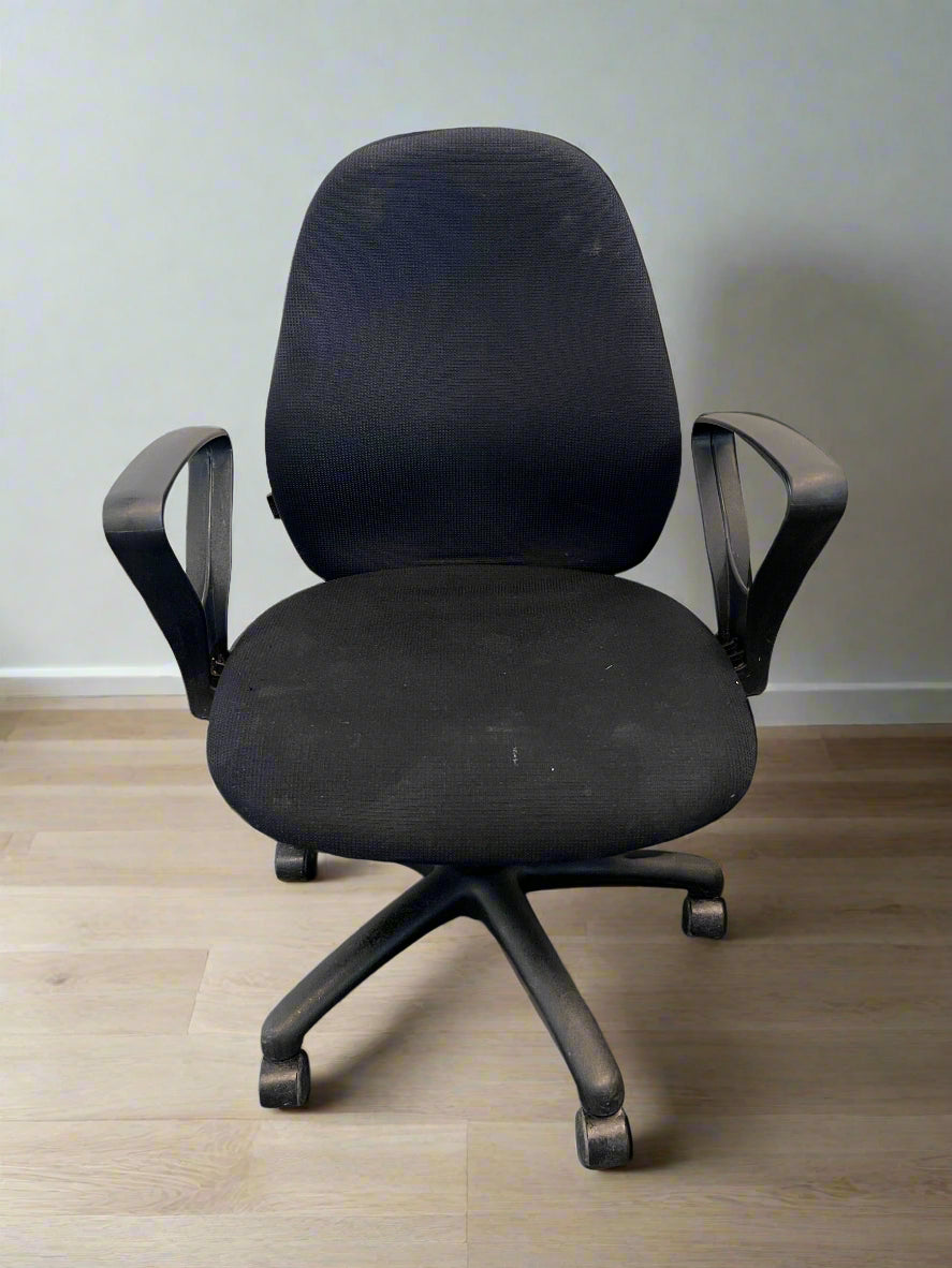 Black office chair on a wooden floor with a plain wall background