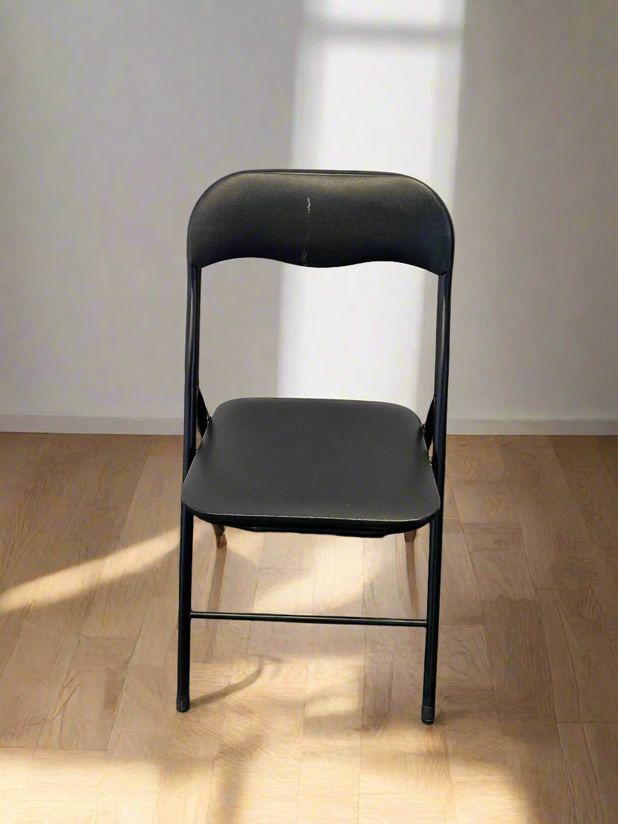 Black folding chair on a wooden floor with a white wall background