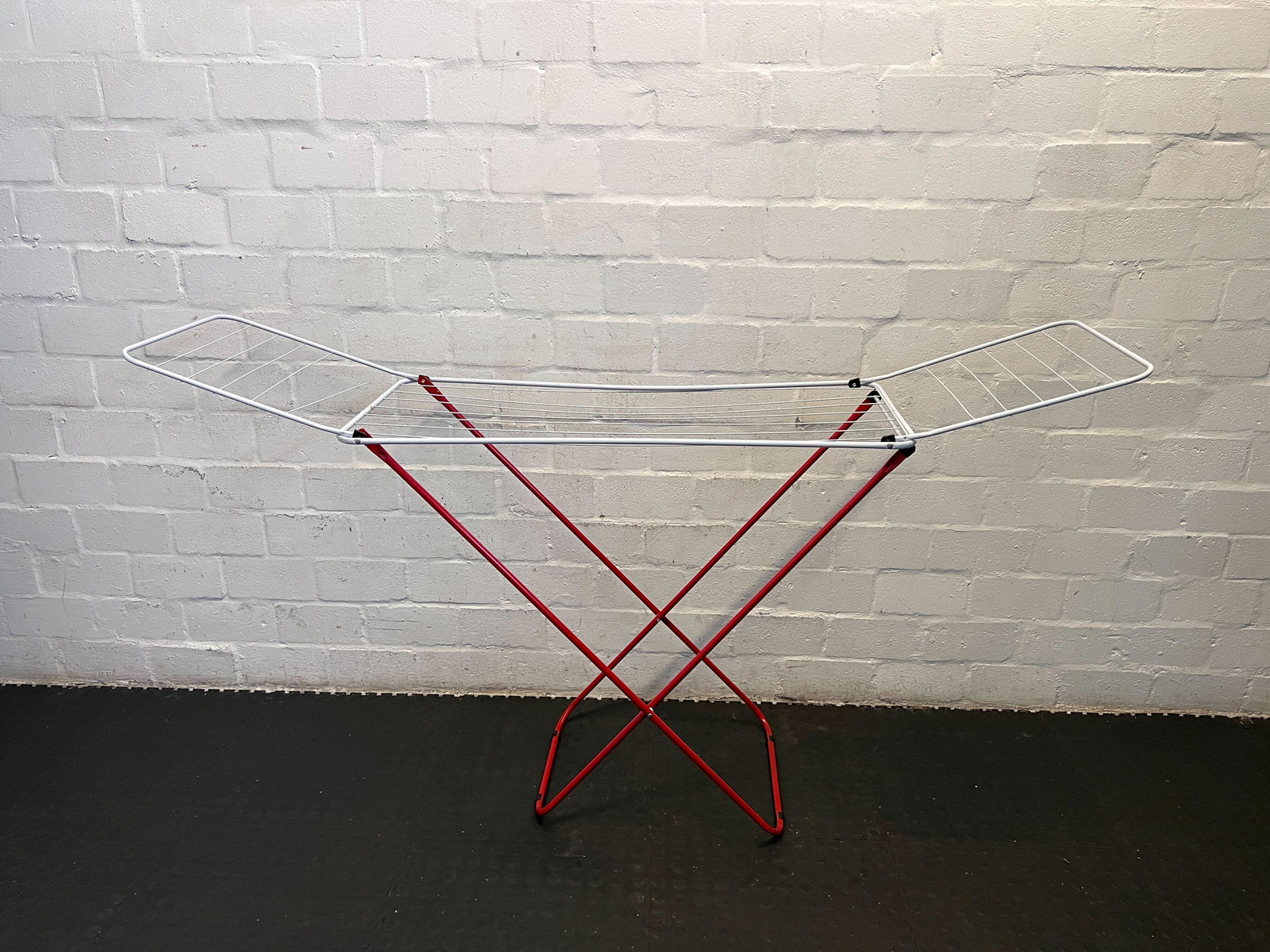Metal drying rack with red legs against a white brick wall.