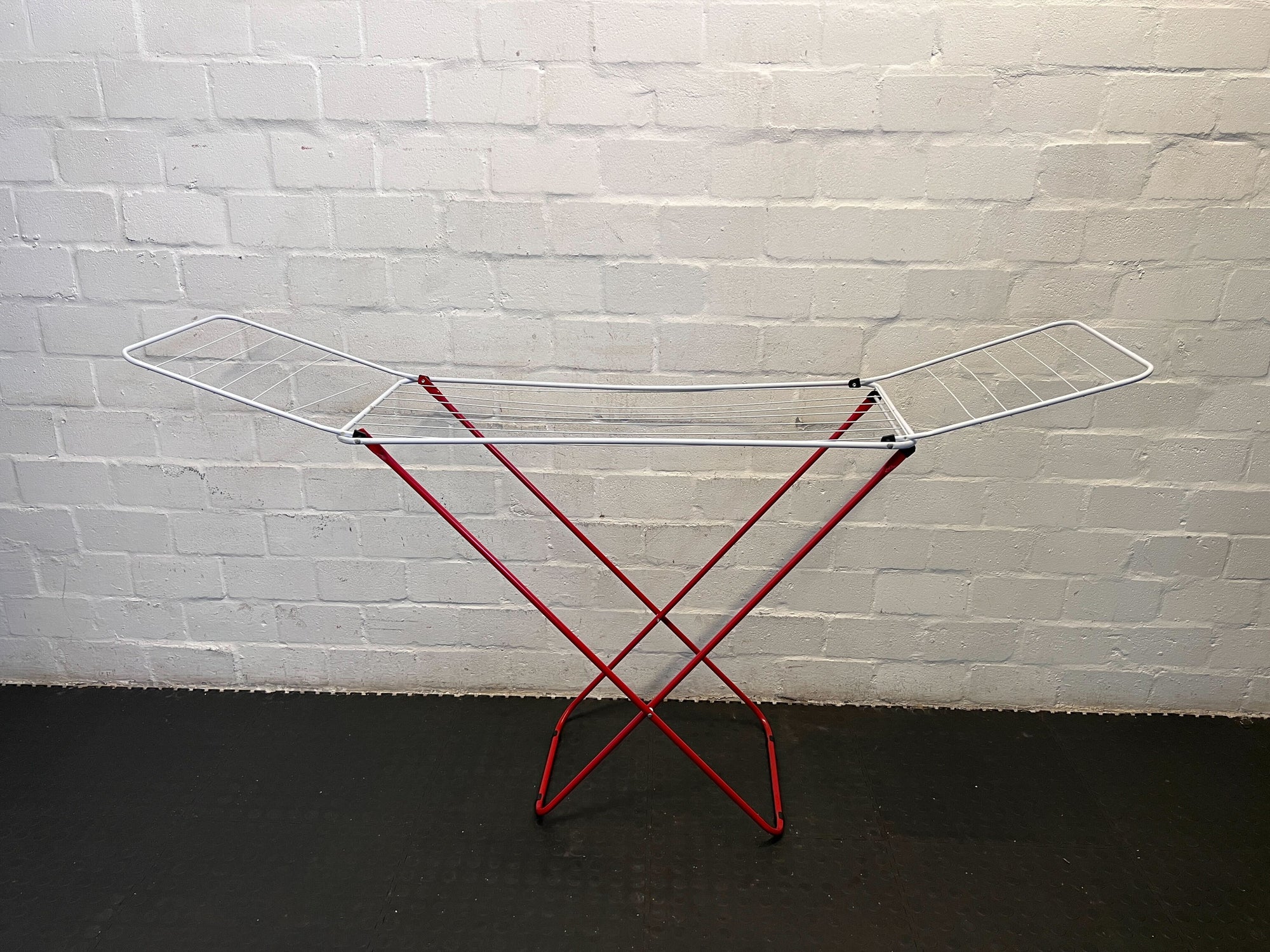 Metal drying rack with red legs against a white brick wall.