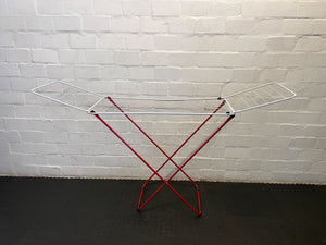 Metal drying rack with red legs against a white brick wall.
