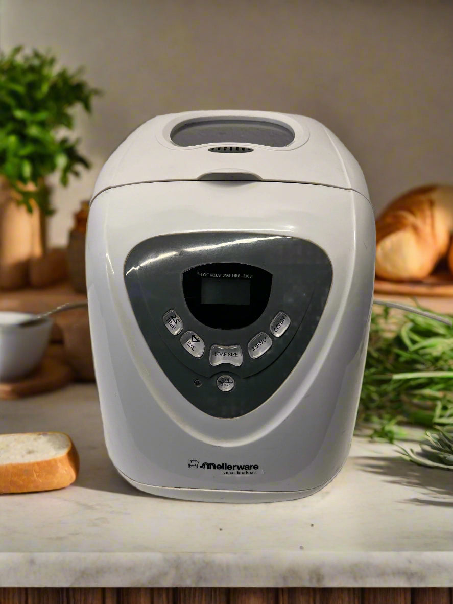 White bread maker on a kitchen counter with bread and herbs in the background