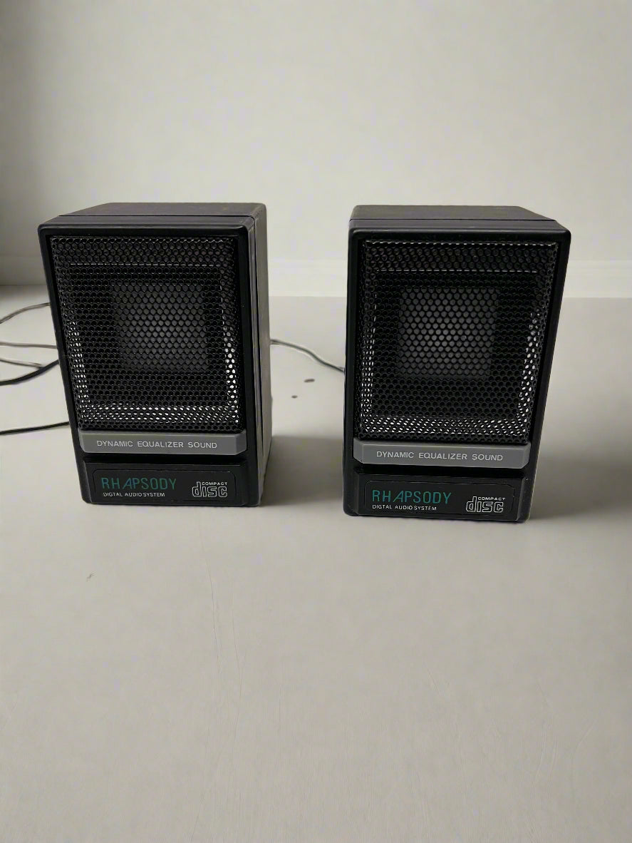 Two black speakers on a light gray surface with a neutral background