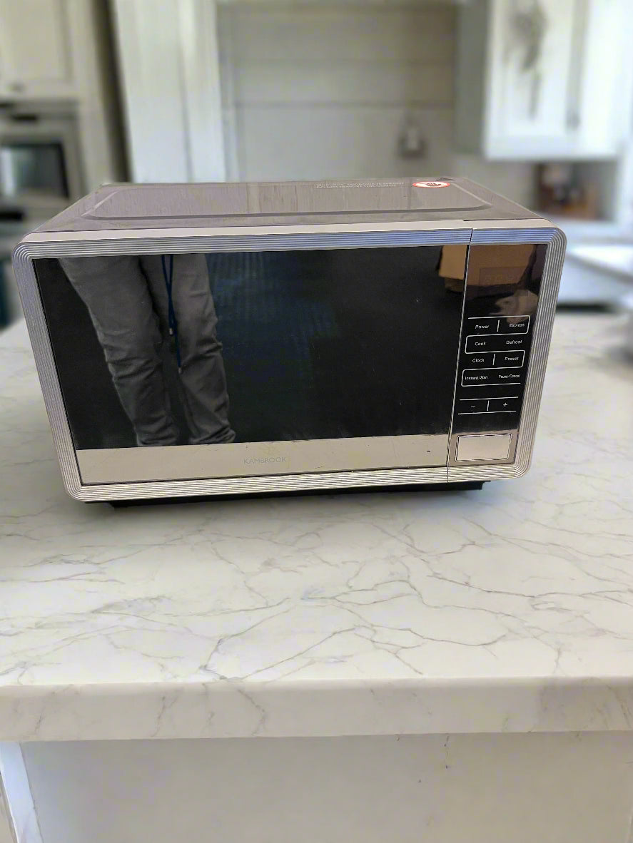 Silver microwave oven on a white surface with a gray brick wall background