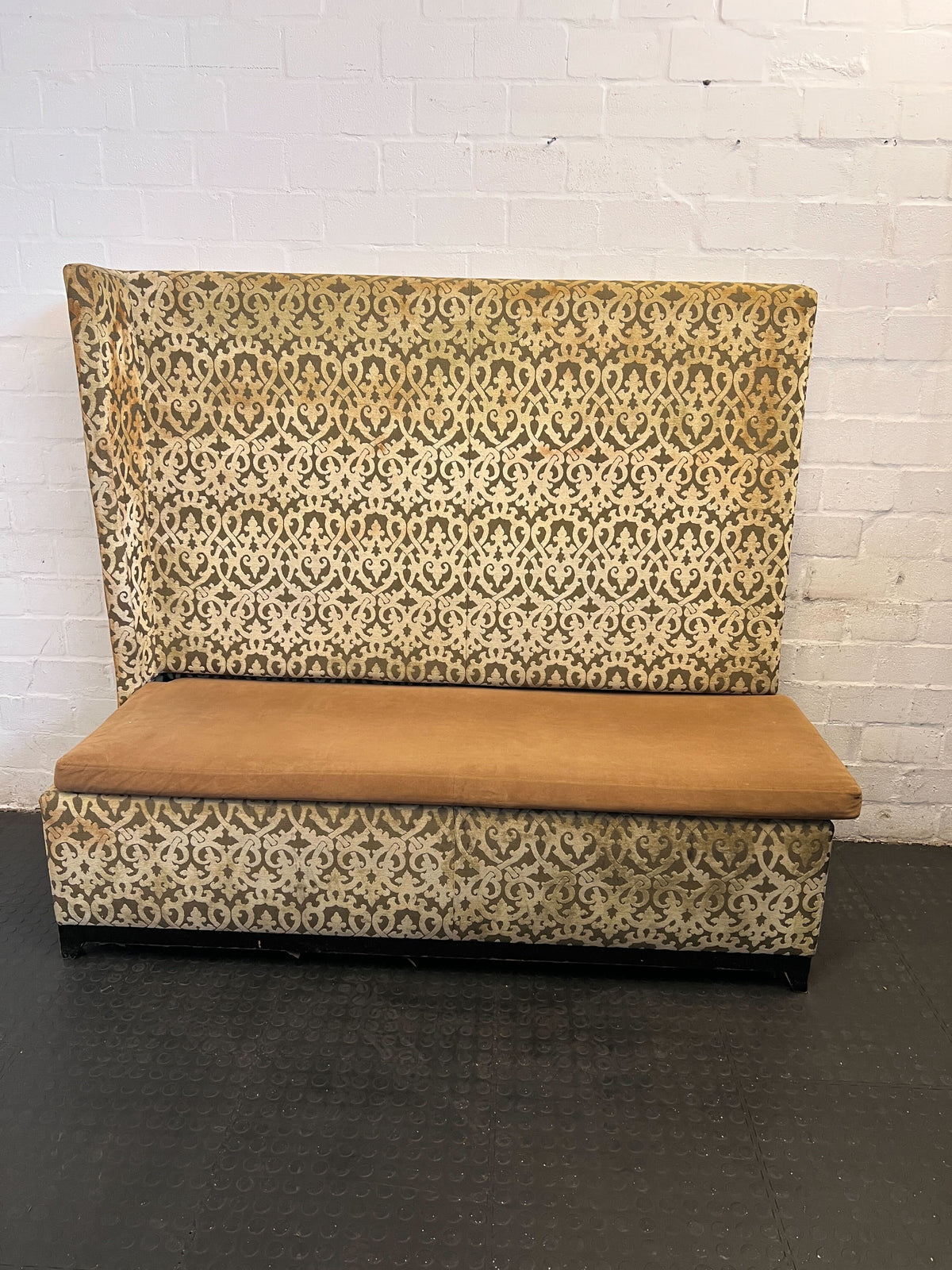 Patterned bench with a brown cushion against a white brick wall.