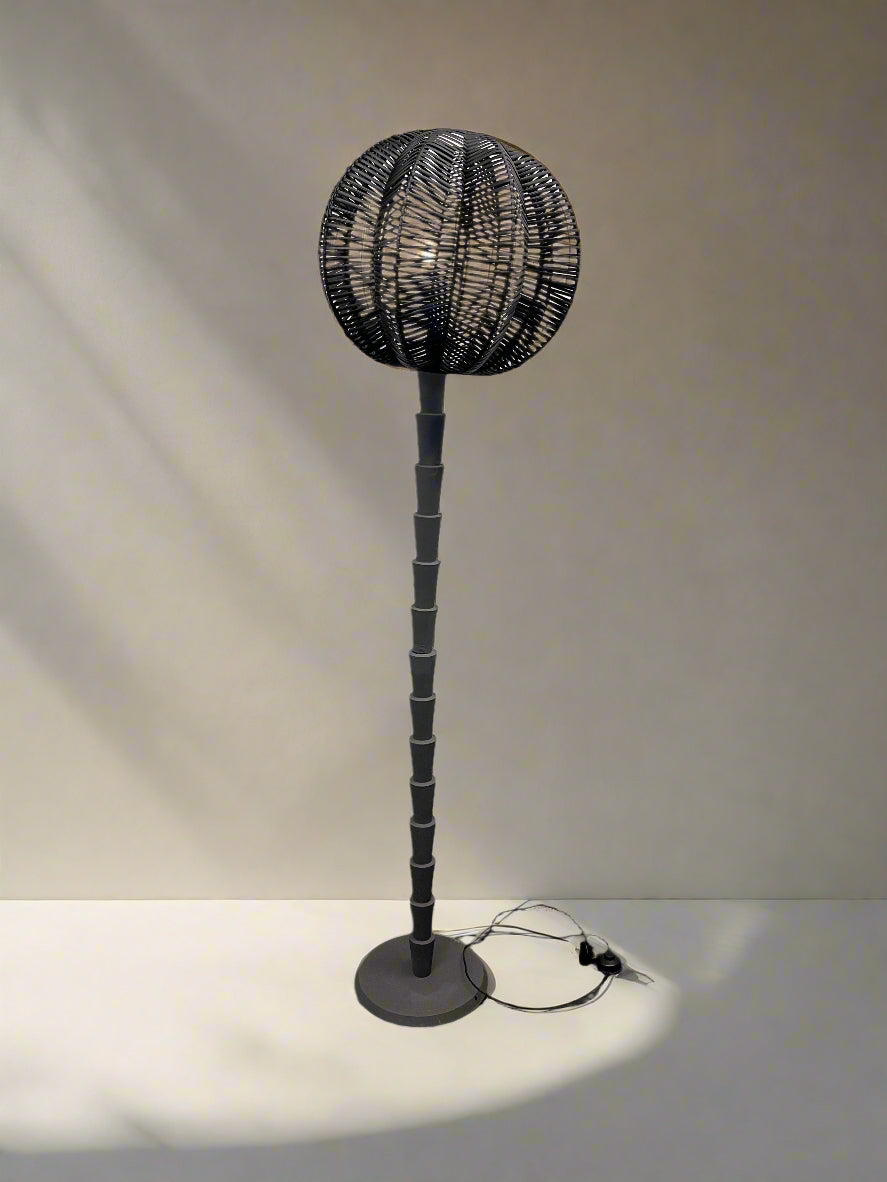 Black floor lamp with wicker design against a white brick wall.