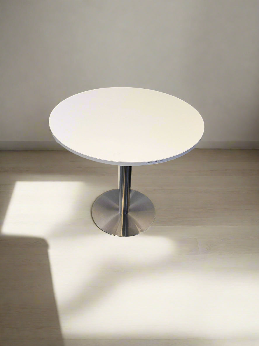 Small round table with a white top and metallic base on a neutral background