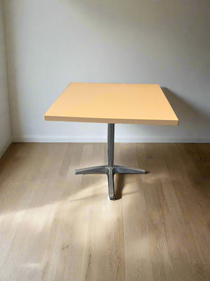 Wooden table with metal base on a wooden floor against a white wall