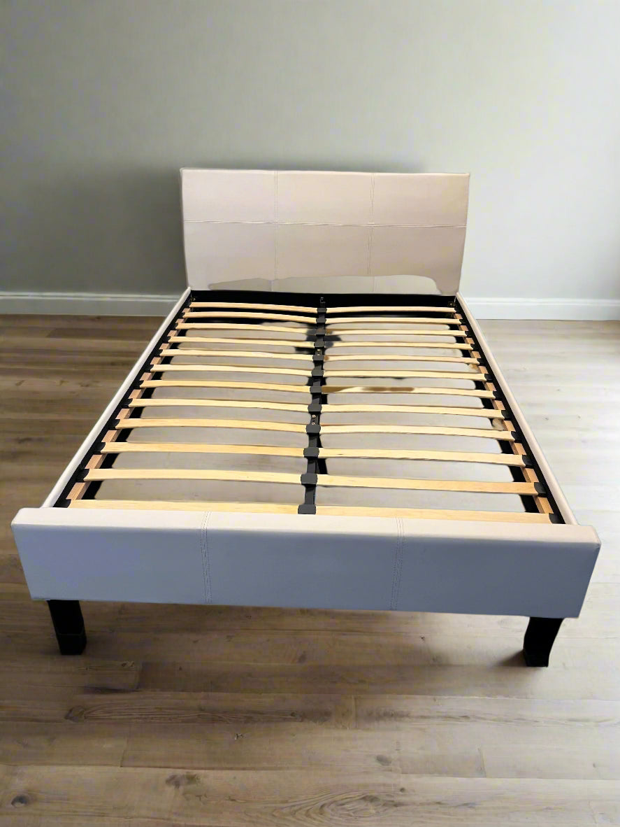 White bed frame with wooden slats against a white brick wall.