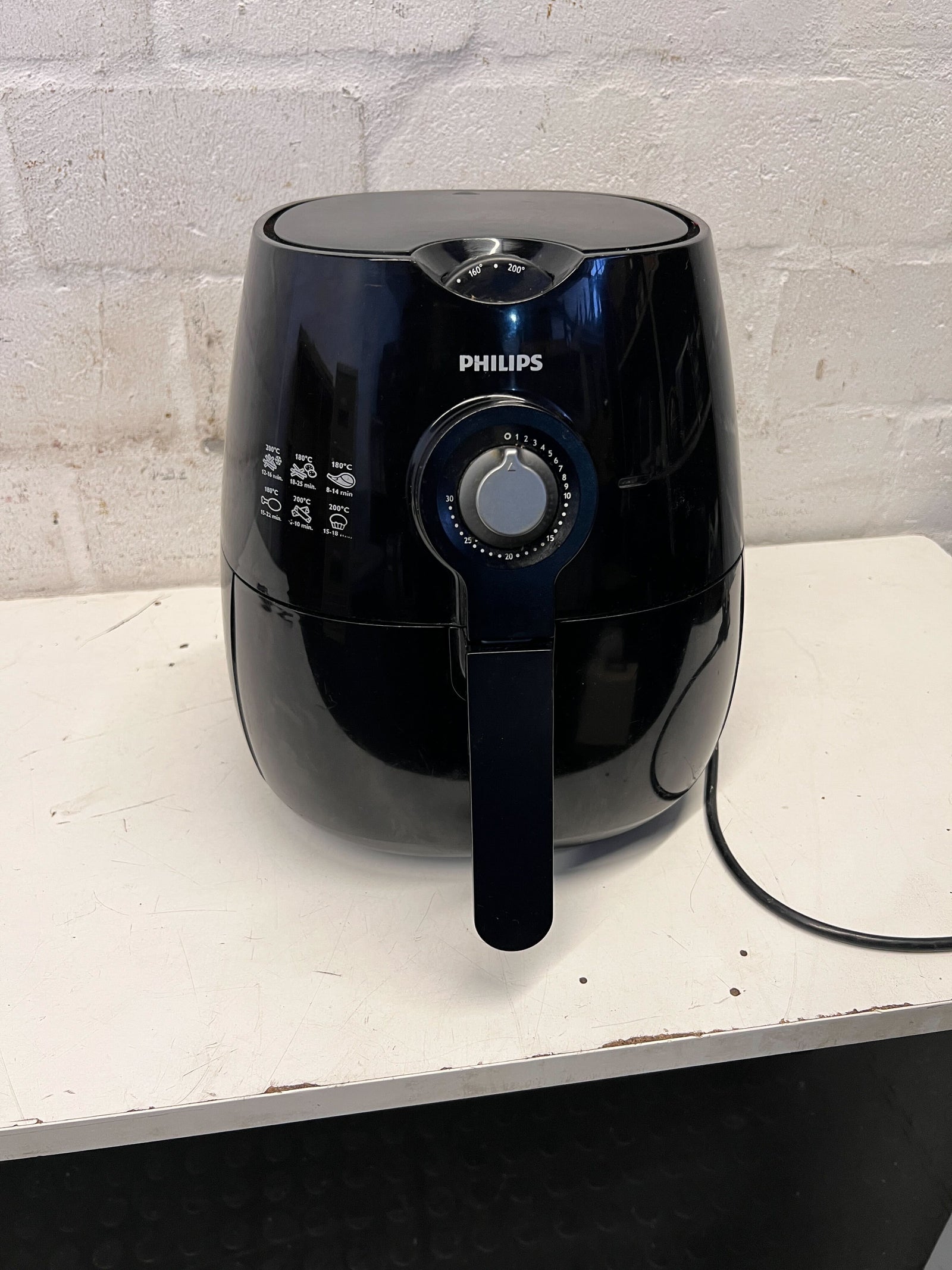 Black Philips air fryer on a white surface with a light gray brick wall background
