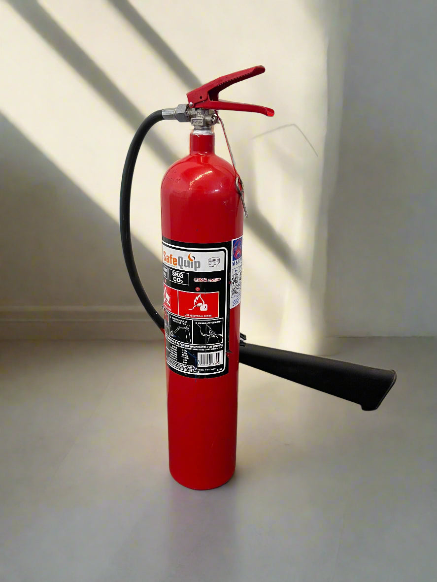 Red fire extinguisher on a light gray surface with a white wall background