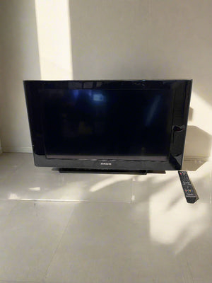Black Samsung TV on a white table with a brick wall background